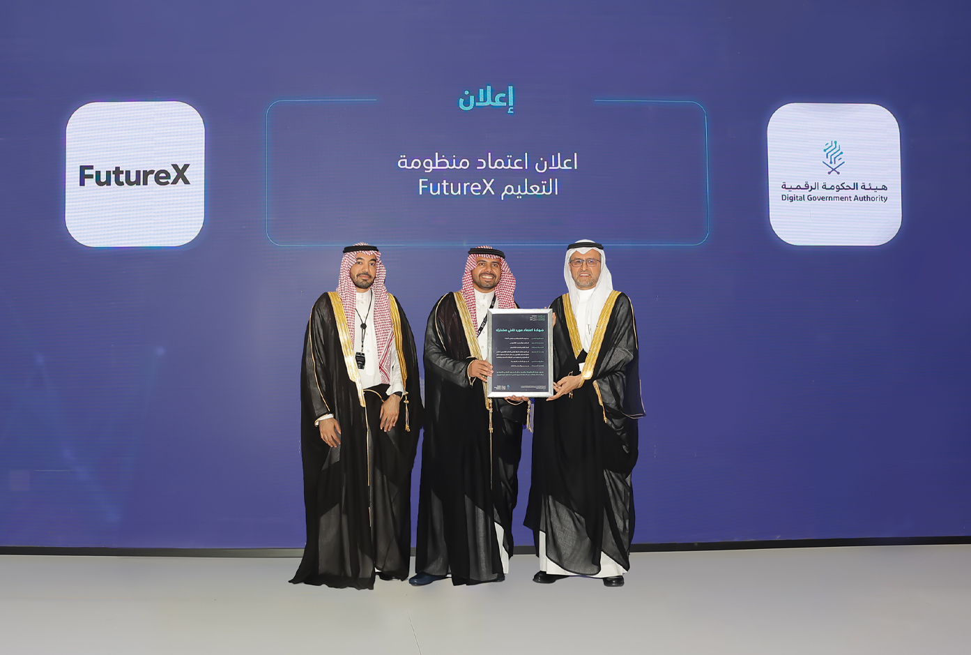 صورة تعكس تسليم المهندس أحمد الصويان شهادة اعتماد منظومة FutureX كمورد تقني مشترك إلى مدير عام المركز الدكتور عبدالله الوليدي، إلى جانب رجل. 