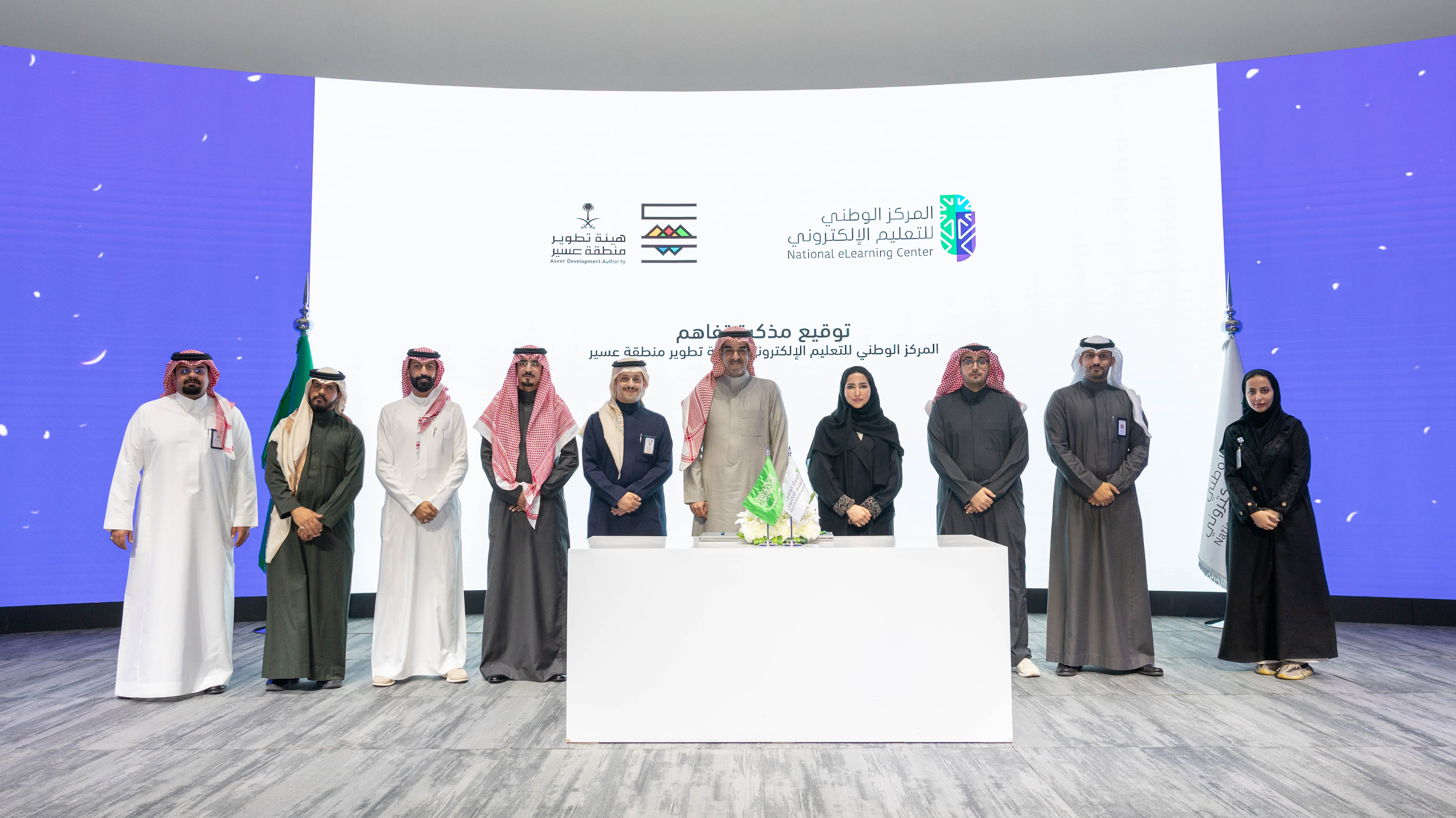 صورة لتوقيع مذكرة تفاهم بين المركز الوطني للتعليم الإلكتروني و هيئة تطوير منطقة عسير، توضح سعادة الدكتورة هاجر بن عصفور، وسعادة الدكتور عمرو العمري، إلى جانب 7 رجال، وامرأة.